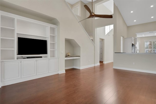 unfurnished living room featuring dark wood-style flooring, ceiling fan, a towering ceiling, and baseboards