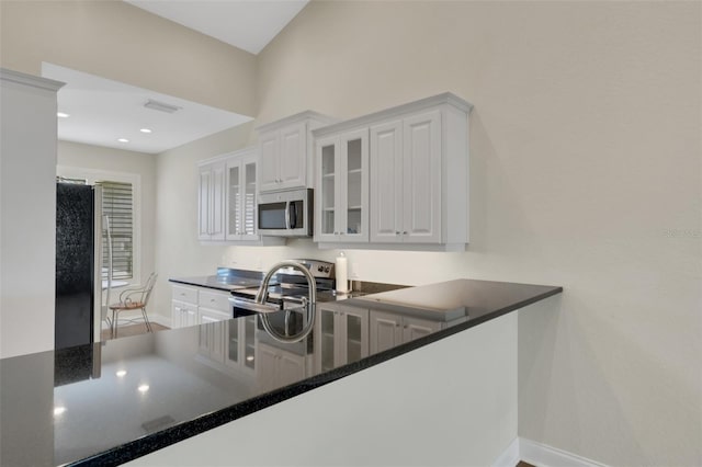 kitchen with dark countertops, visible vents, glass insert cabinets, and stainless steel appliances