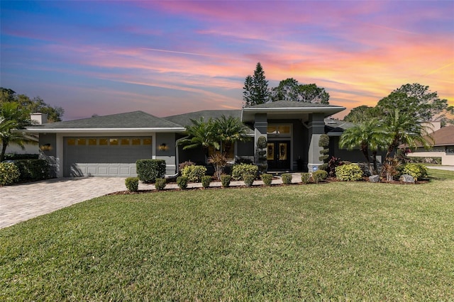 prairie-style home with a garage, french doors, decorative driveway, a yard, and stucco siding