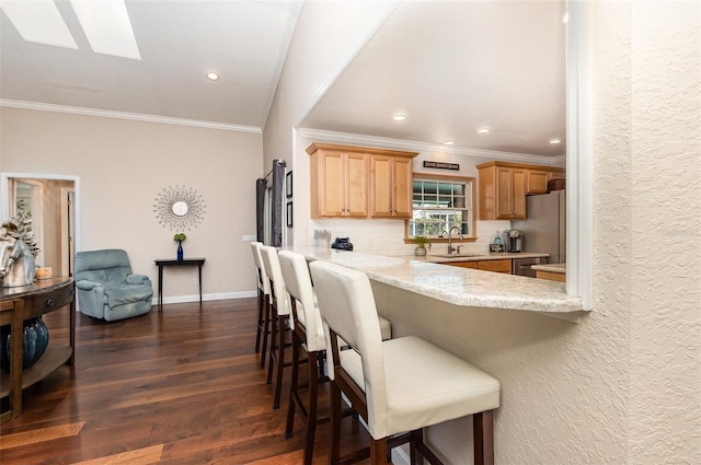 kitchen with a breakfast bar area, dark wood-style flooring, freestanding refrigerator, a sink, and backsplash