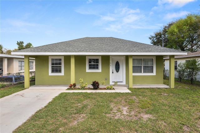 view of front of home with roof with shingles, a front yard, fence, and stucco siding