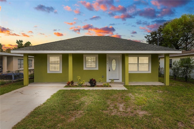 view of front facade with a yard, roof with shingles, fence, and stucco siding