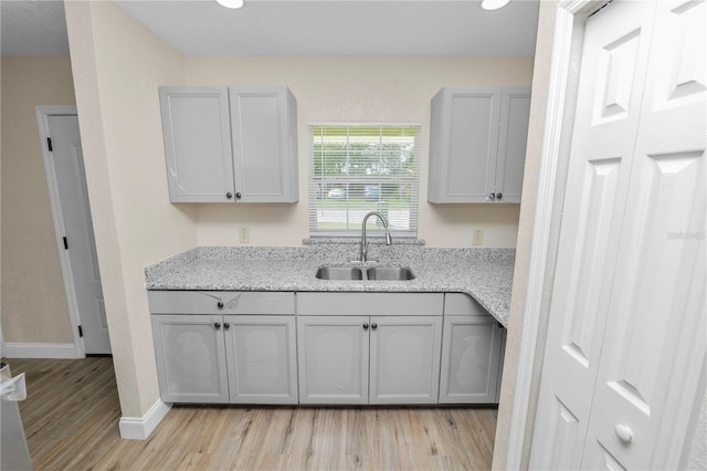 kitchen featuring gray cabinetry, light wood finished floors, a sink, and light stone countertops