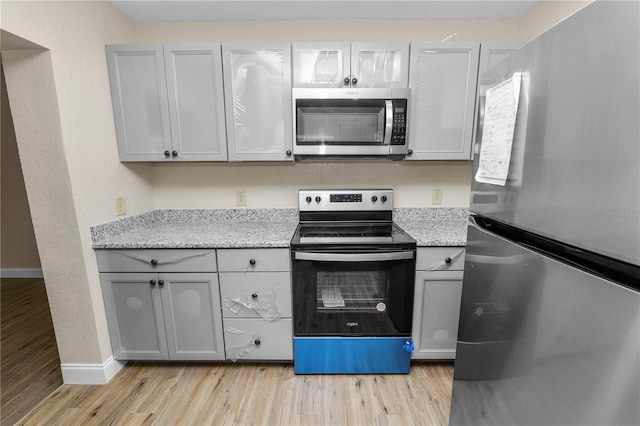 kitchen featuring gray cabinetry, stainless steel appliances, light stone counters, and light wood-style floors