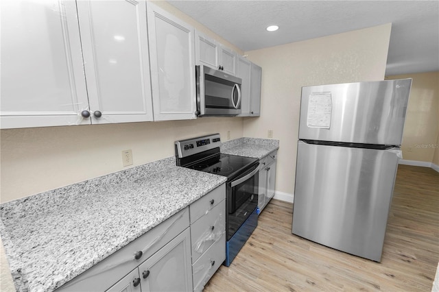 kitchen featuring light wood-style flooring, baseboards, stainless steel appliances, and light stone counters