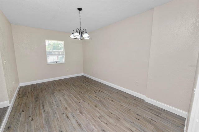 spare room with a notable chandelier, wood finished floors, and baseboards