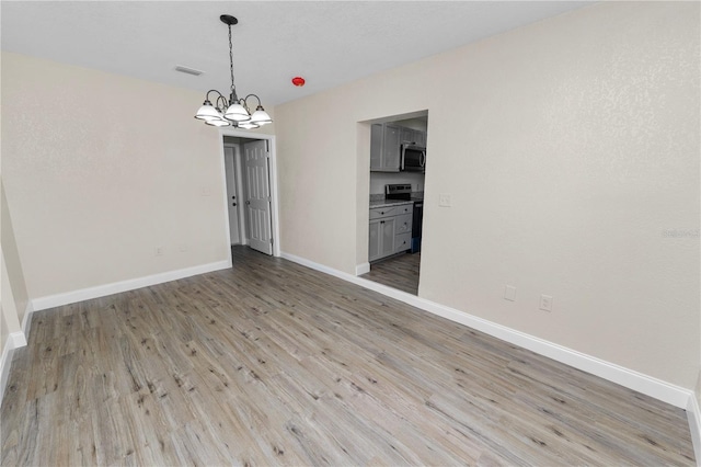 unfurnished dining area featuring light wood-type flooring, baseboards, visible vents, and a notable chandelier