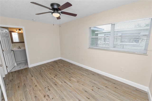 unfurnished bedroom featuring ensuite bathroom, ceiling fan, light wood finished floors, and baseboards