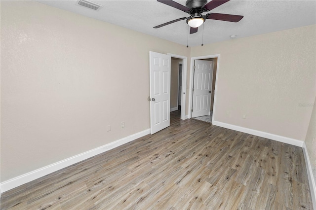 empty room with light wood finished floors, a ceiling fan, visible vents, and baseboards