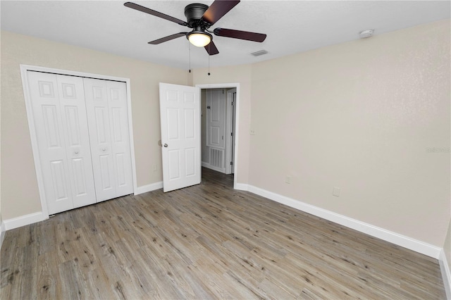 unfurnished bedroom featuring wood finished floors, a ceiling fan, visible vents, baseboards, and a closet