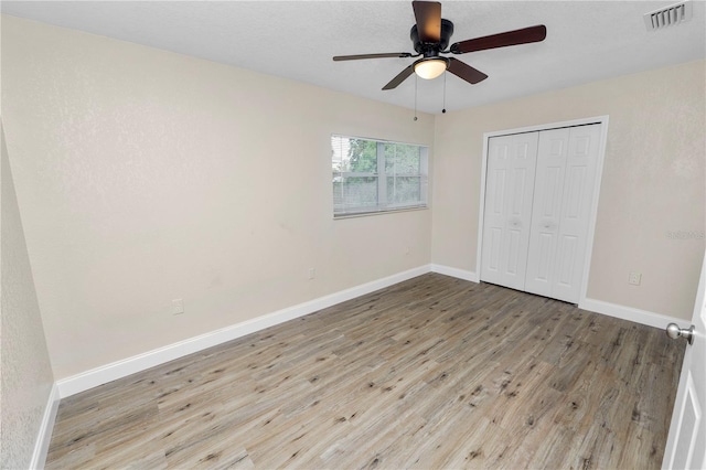 unfurnished bedroom featuring ceiling fan, wood finished floors, visible vents, baseboards, and a closet