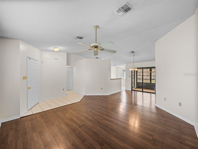 empty room featuring ceiling fan with notable chandelier, wood finished floors, and visible vents