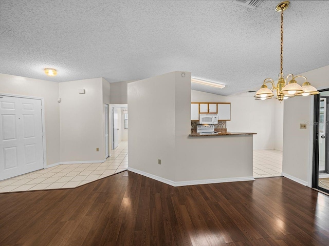 unfurnished living room featuring baseboards, lofted ceiling, wood finished floors, a textured ceiling, and a notable chandelier