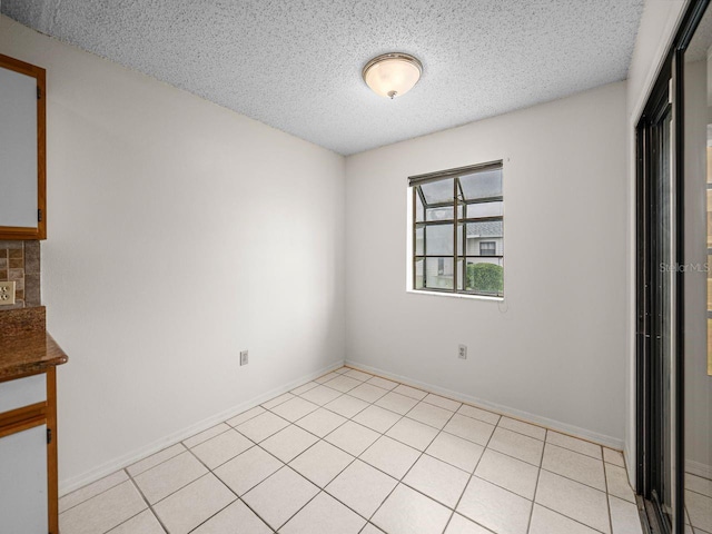 unfurnished room with a textured ceiling, light tile patterned floors, and baseboards