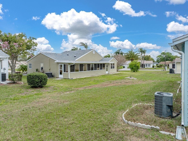 back of property featuring a yard, roof with shingles, a sunroom, and central air condition unit