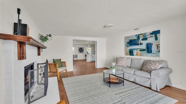 living room with a textured ceiling, a brick fireplace, wood finished floors, and baseboards