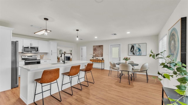 kitchen with light wood-style flooring, a breakfast bar, a sink, white cabinets, and appliances with stainless steel finishes