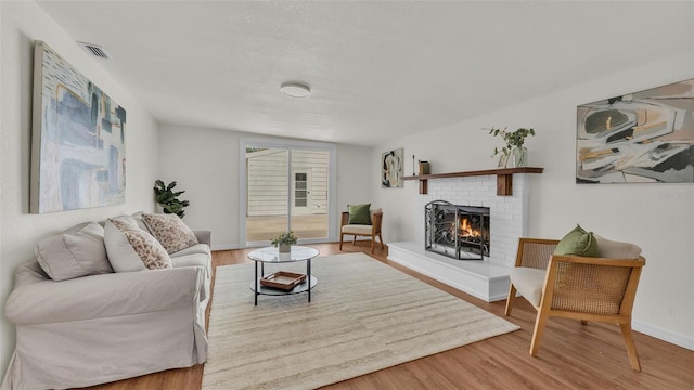 living area featuring a fireplace, wood finished floors, visible vents, and baseboards