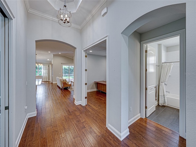 hallway featuring baseboards, ornamental molding, arched walkways, a notable chandelier, and dark wood-style flooring