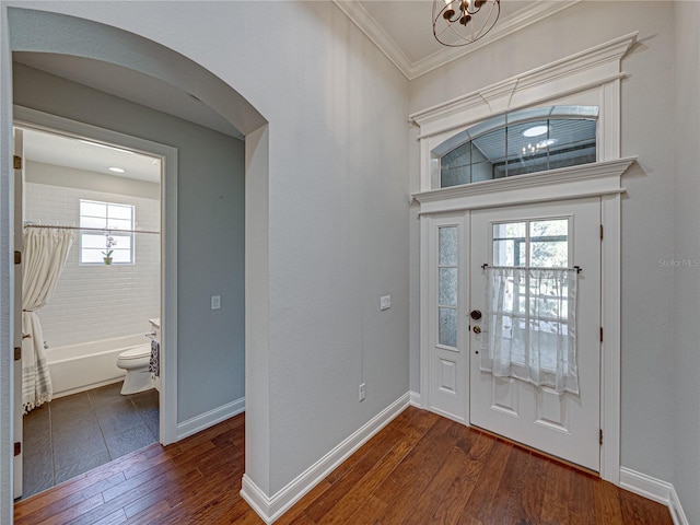 foyer entrance featuring arched walkways, crown molding, dark wood-type flooring, and baseboards