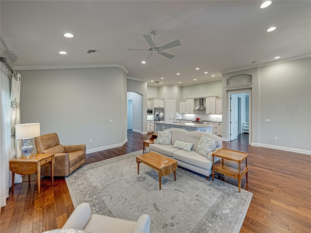 living room with arched walkways, visible vents, ornamental molding, and wood finished floors