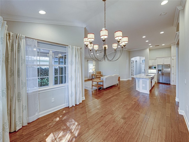 unfurnished dining area featuring ornamental molding, a sink, arched walkways, light wood-style floors, and baseboards