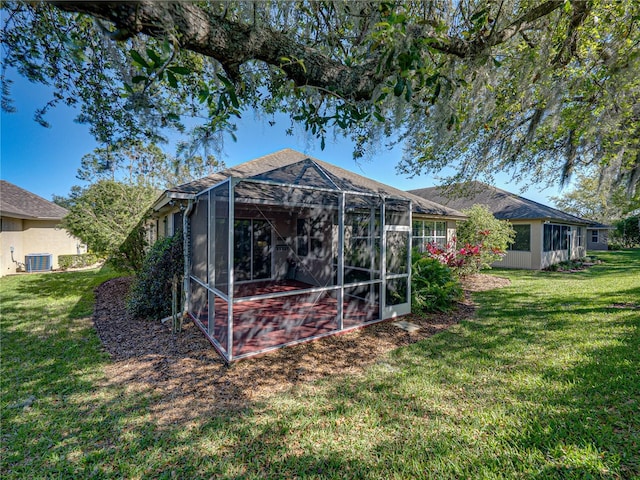 back of property with a lawn, central AC unit, and a lanai