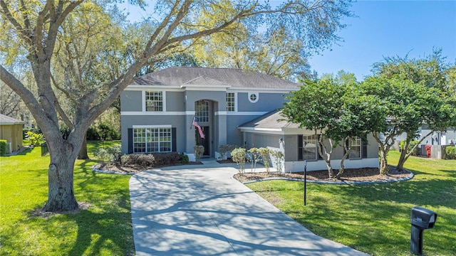 view of front of property featuring roof with shingles, a front lawn, concrete driveway, and stucco siding