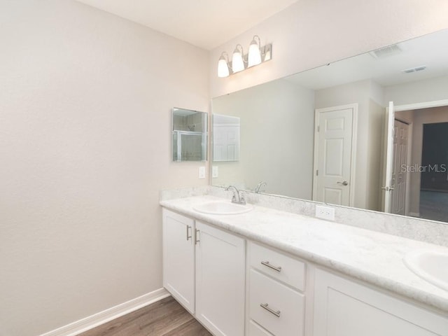 full bath with double vanity, baseboards, a sink, and wood finished floors