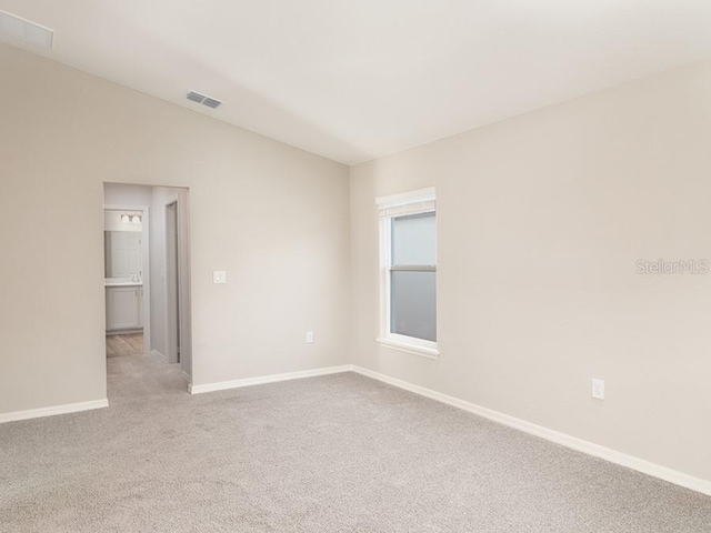 unfurnished room featuring vaulted ceiling, baseboards, visible vents, and light colored carpet