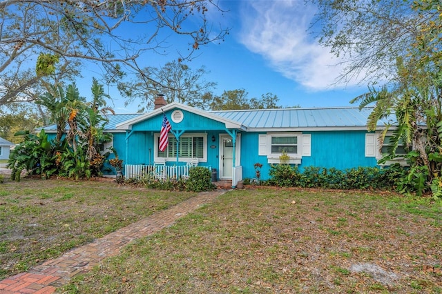 view of front of house featuring metal roof, a chimney, a porch, and a front yard