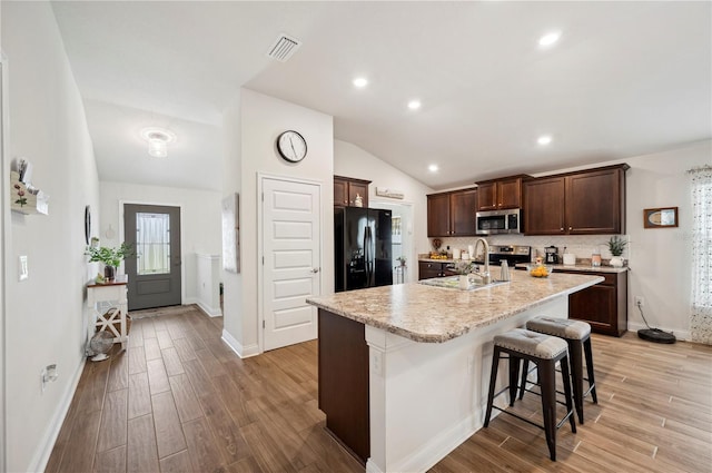 kitchen with lofted ceiling, stainless steel appliances, a sink, visible vents, and dark brown cabinets