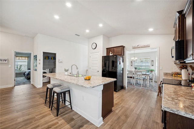 kitchen with a center island with sink, vaulted ceiling, black fridge, light wood-type flooring, and a sink