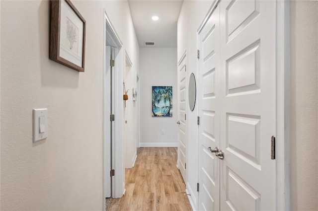 hallway featuring light wood finished floors, baseboards, visible vents, and recessed lighting