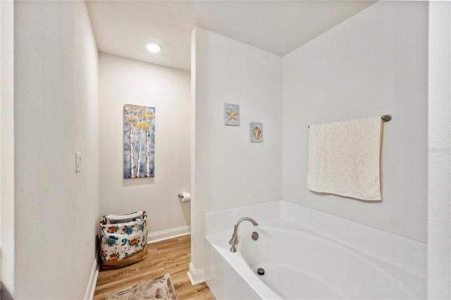 bathroom with wood finished floors, a bath, and baseboards