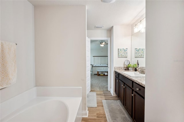 ensuite bathroom featuring visible vents, connected bathroom, vanity, wood finished floors, and a bath