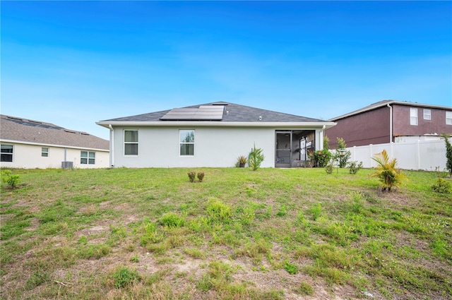 back of property featuring stucco siding, solar panels, a lawn, a sunroom, and fence