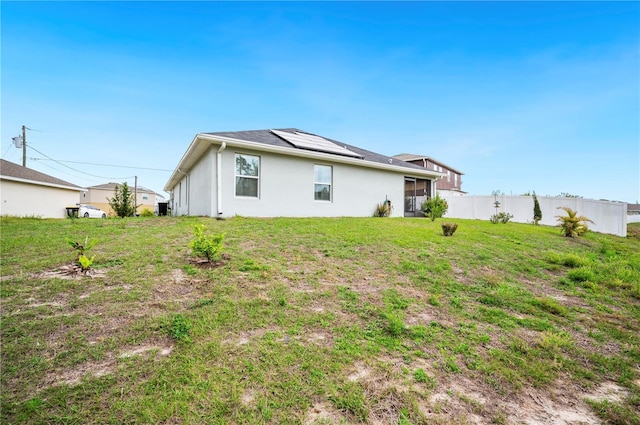 rear view of property featuring roof mounted solar panels, stucco siding, a lawn, and fence