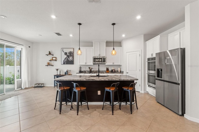 kitchen with light stone counters, stainless steel appliances, a sink, visible vents, and white cabinets