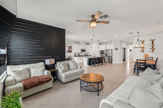 living area featuring light tile patterned floors, recessed lighting, visible vents, an accent wall, and ceiling fan with notable chandelier