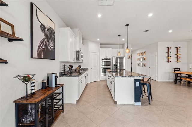 kitchen with a center island with sink, white cabinets, a breakfast bar, dark stone countertops, and stainless steel appliances