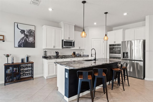 kitchen with a breakfast bar, a sink, visible vents, appliances with stainless steel finishes, and dark stone countertops