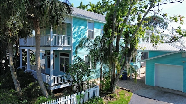 view of front facade with a balcony, metal roof, aphalt driveway, fence, and a porch