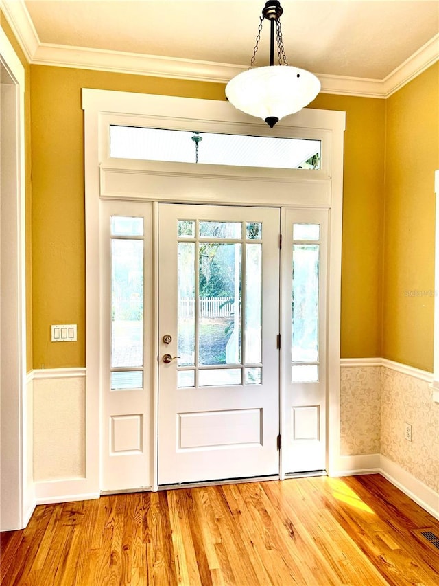 entrance foyer featuring a wainscoted wall, crown molding, wood finished floors, baseboards, and wallpapered walls