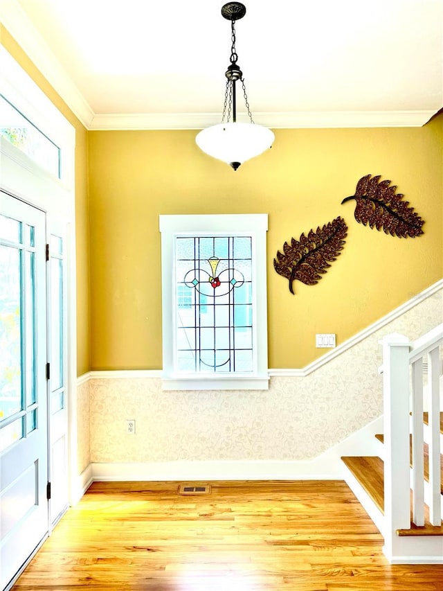 entryway featuring a wainscoted wall, light wood-style flooring, visible vents, and ornamental molding