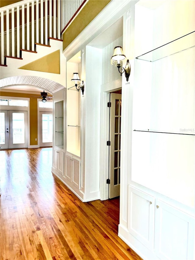 corridor with a towering ceiling, light wood-style floors, arched walkways, and french doors