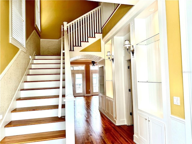 staircase with a towering ceiling, arched walkways, and wood finished floors