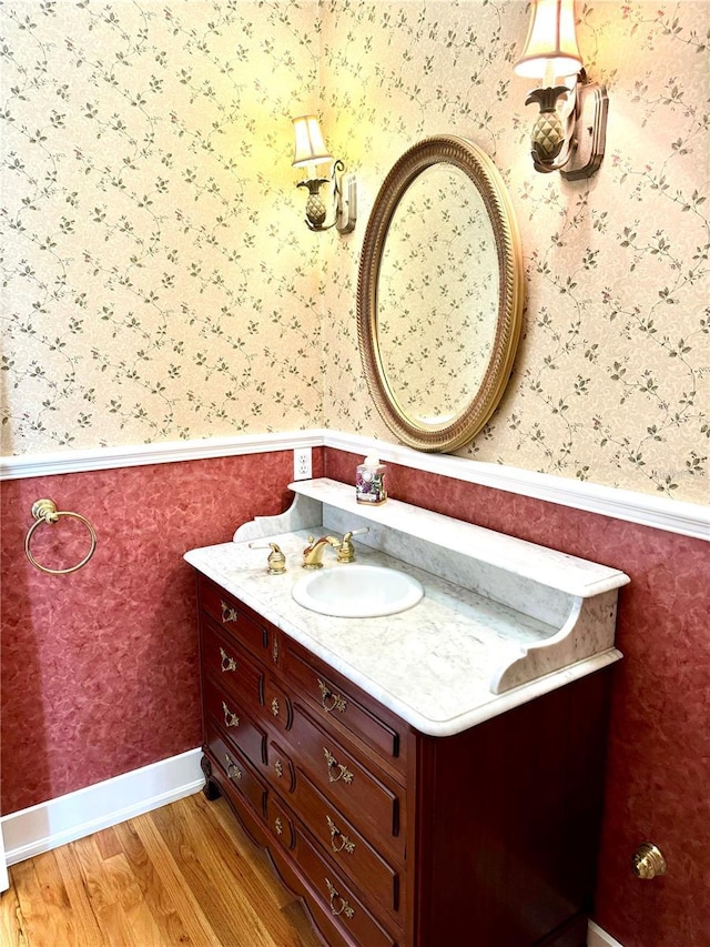 bathroom featuring wallpapered walls, baseboards, a wainscoted wall, wood finished floors, and vanity