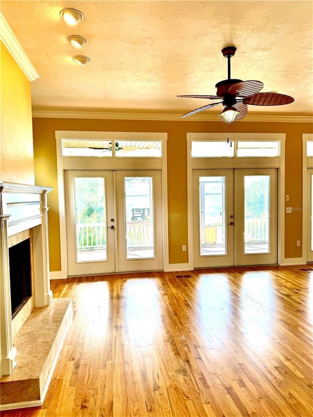 unfurnished living room with french doors, a fireplace, crown molding, and wood finished floors