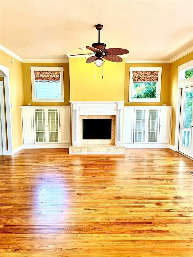 unfurnished living room featuring light wood finished floors, ceiling fan, ornamental molding, and a high end fireplace